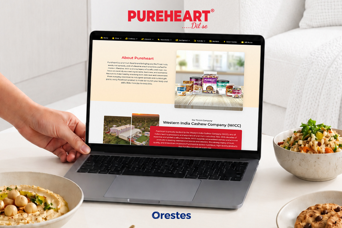 Laptop screen displaying the Pureheart "About Us" and parent company brand story page, set on a dining table with premium food bowls.